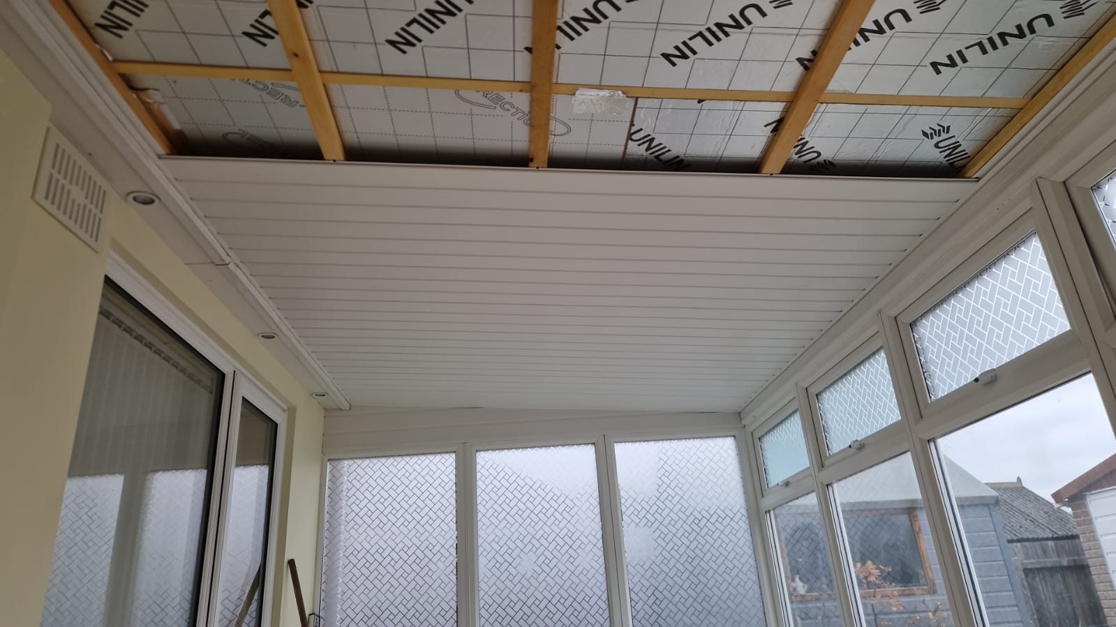 Inside a conservatory during a roof conversion, insulated boards fitted between the rafters