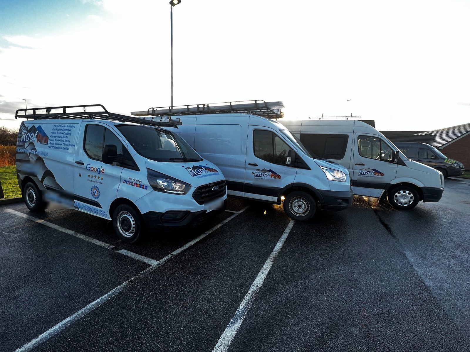 Three white Roof Pro vans parked together, the front one in the blue and orange RoofPro livery